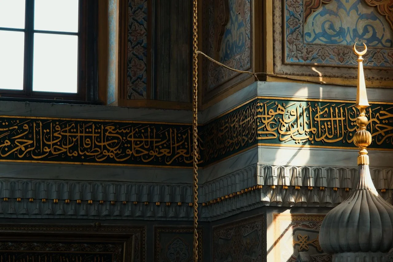 History of Islam: Intricate Arabic calligraphy adorns the ornamental walls of a mosque, illuminated by sunlight.